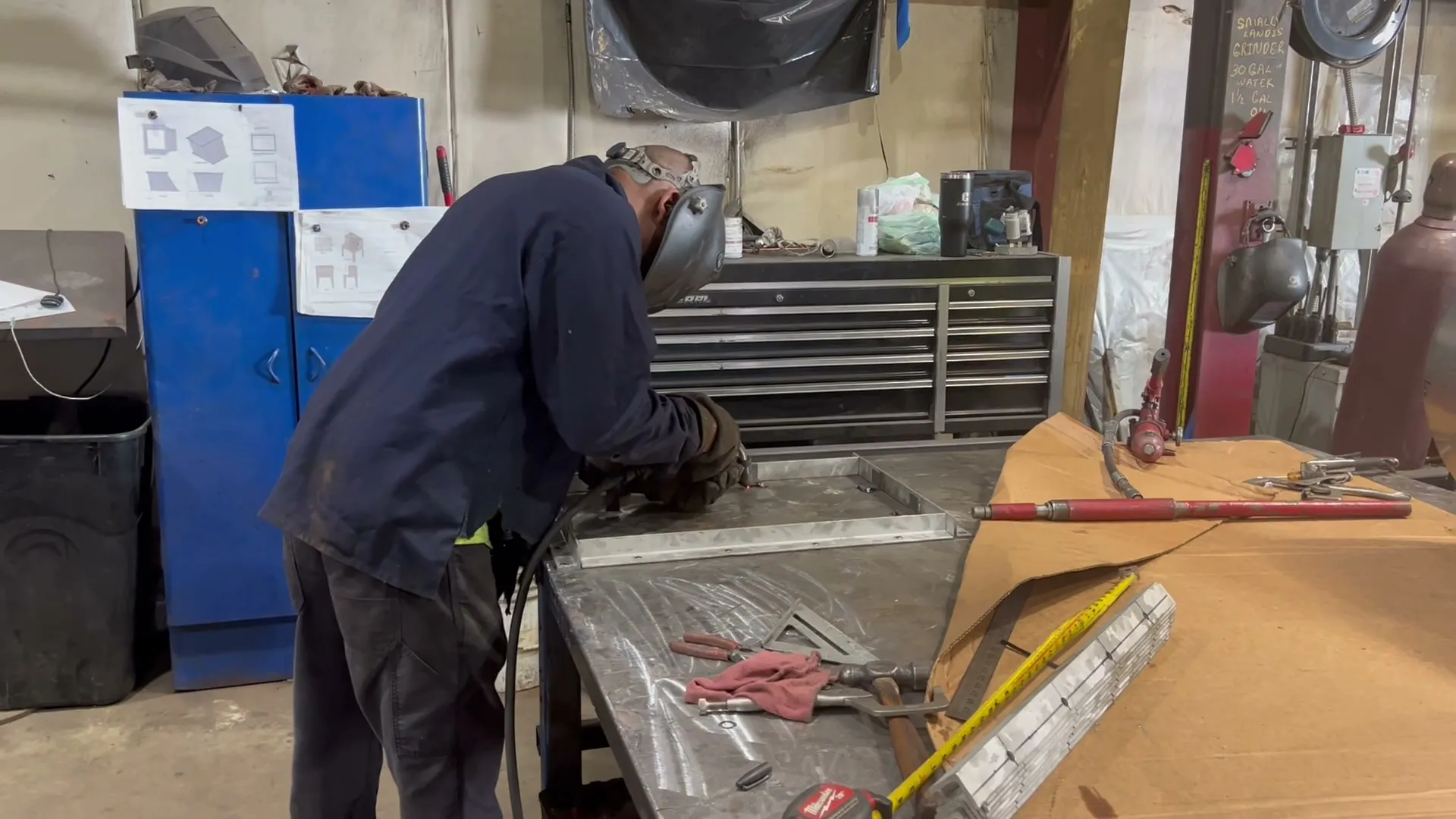 A DCG fabricator welding a rectangular sheet-metal transition laid out on the shop bench, hand tools and a square beside it.