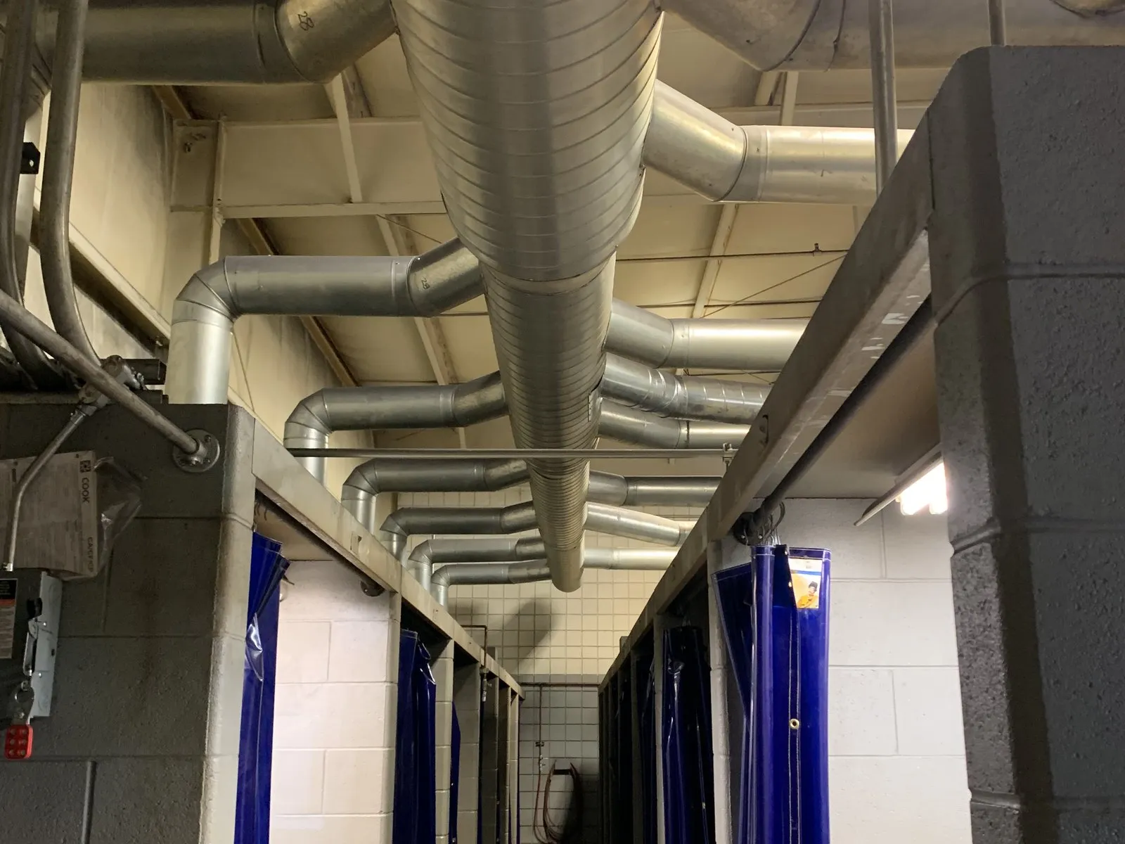 Spiral ductwork running the length of a tiled process room, with capture branches dropping into each curtained bay.