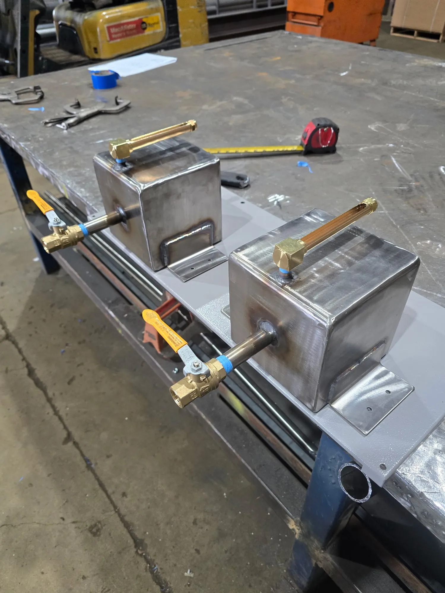 Two small fabricated stainless assemblies with brass ball valves, set up on a shop bench beside a tape measure.