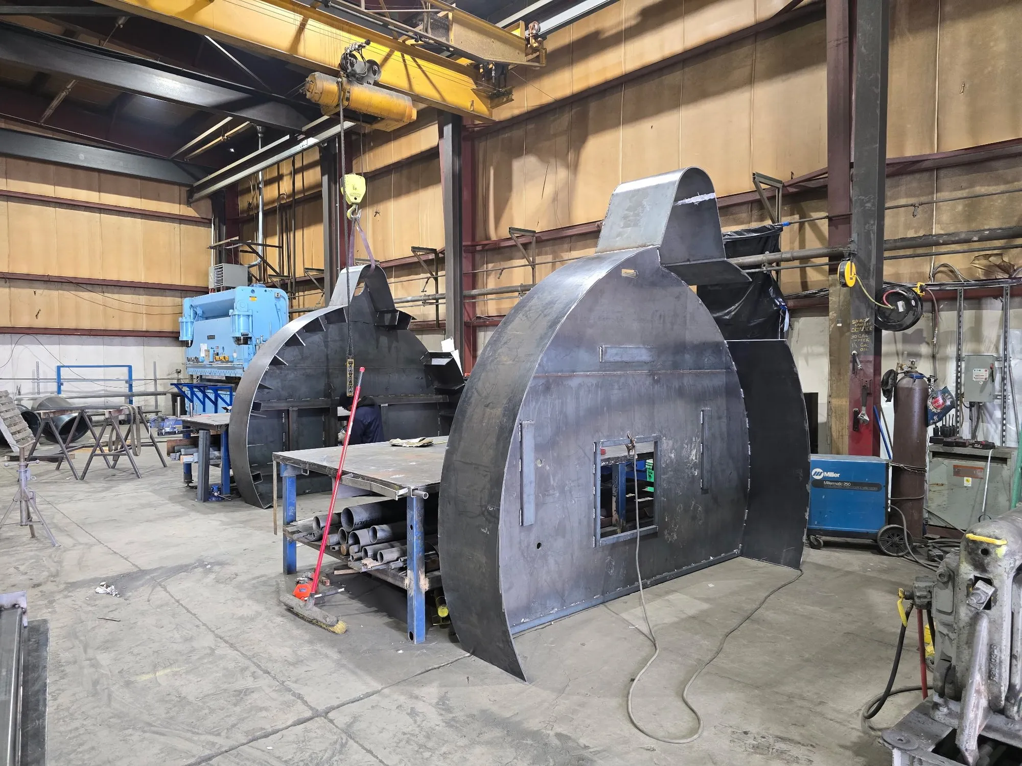 Two large round furnace lids under fabrication on the shop floor, plate skins formed and access doors cut in.