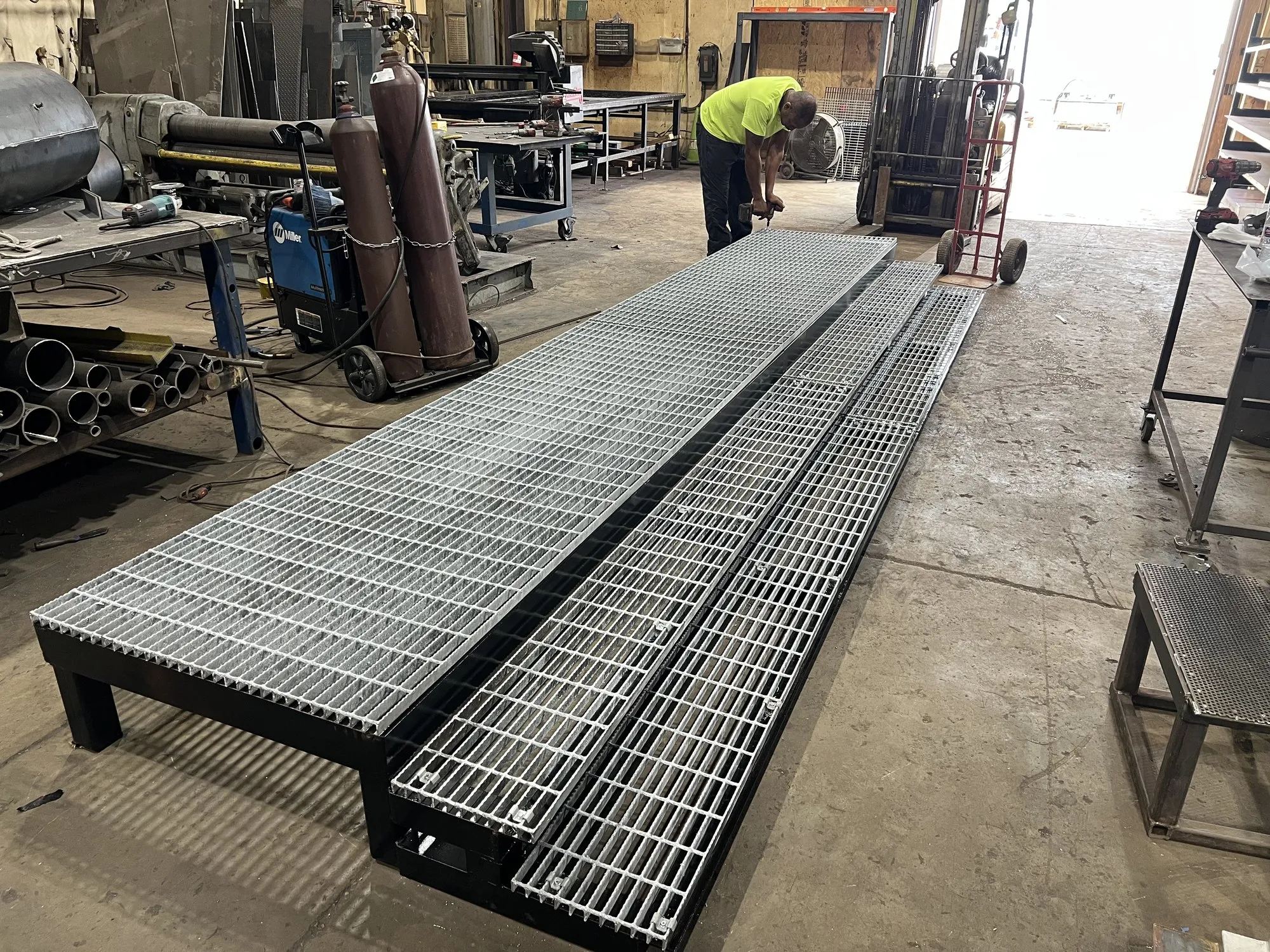 A DCG fabricator assembling a long steel access platform with galvanised grating panels on the shop floor.