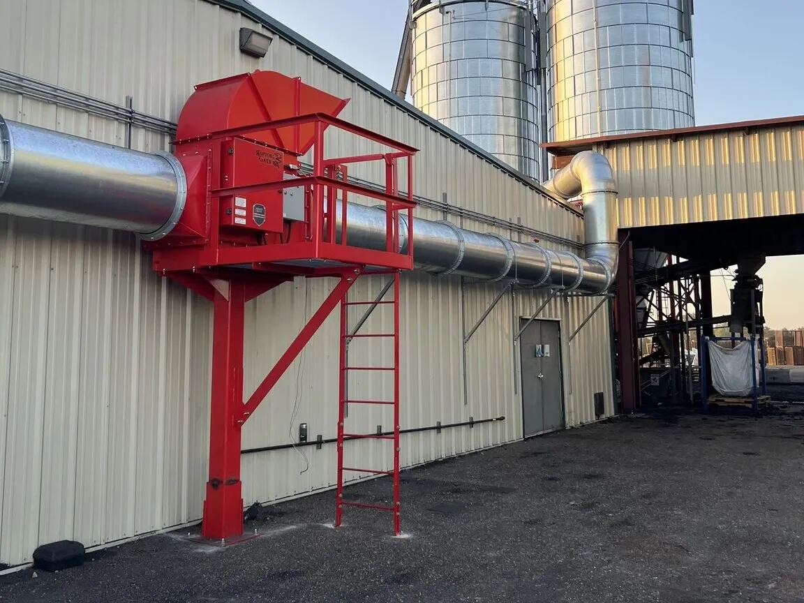 A red high-speed abort gate on wall-mounted ducting outside a plant, with grain silos behind.